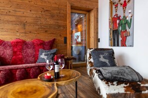 A cozy room with a wooden wall, a red sofa with patterned cushions, a brown and white sofa, and a painting of reindeer on the wall.