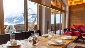 Una mesa de comedor dispuesta con platos, vasos y cubiertos, con vistas a montañas a través de amplios ventanales.