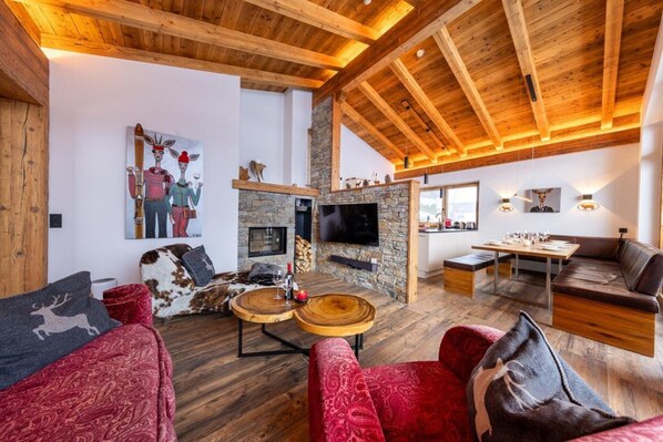 A spacious living area with a stone fireplace, wooden ceiling beams, and a large flat-screen TV.