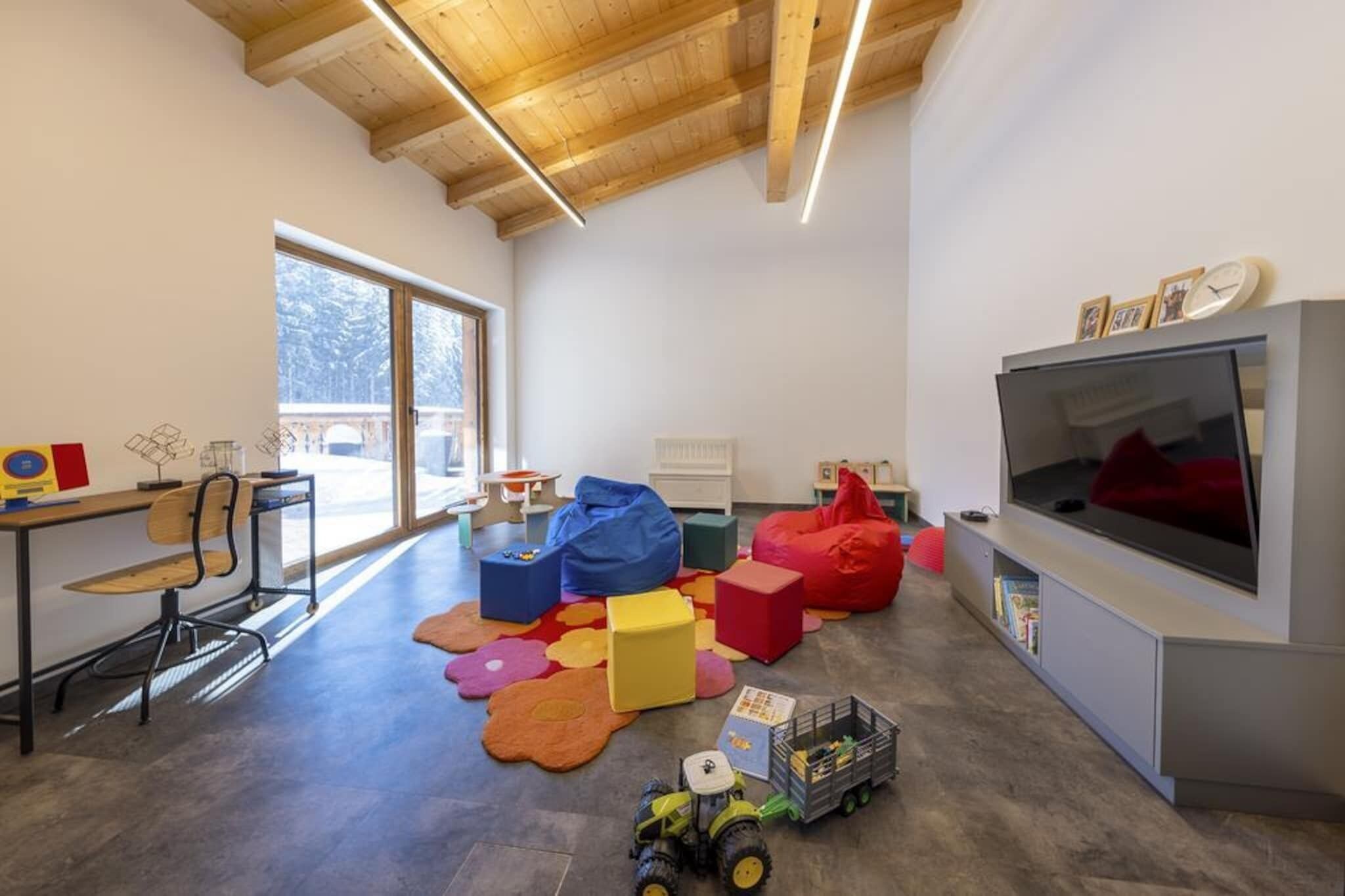 Ein modernes Wohnzimmer mit großem Fernseher, Holzbalkendecke und Blick ins Freie.