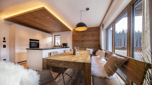 A modern kitchen with white cabinets, a wooden island, and a dining area with a wooden table and chairs.