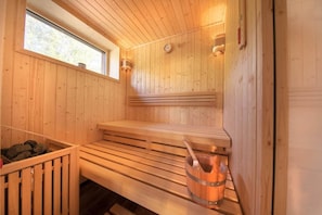 Uma sauna de madeira com bancos, um balde e uma janela.