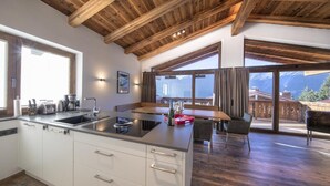 Een moderne keuken met een centraal eiland, houten balken in het plafond en grote ramen met uitzicht op de bergen.