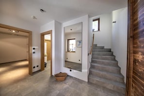 Um interior moderno com uma escada, uma porta de madeira e um espelho refletindo uma janela.
