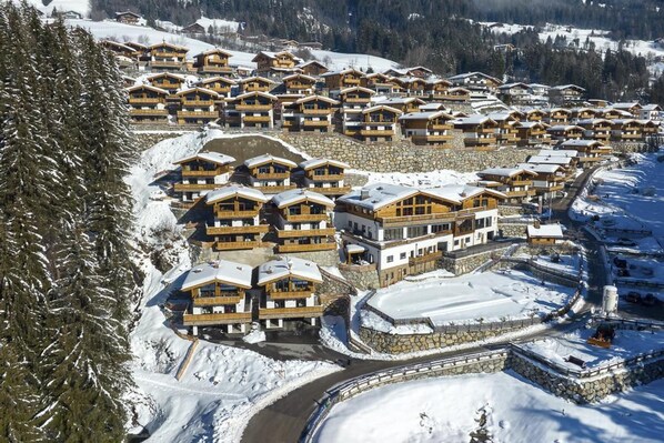 Une station de ski enneigée, dotée de plusieurs chalets en bois, d’un télésiège et d’un mur de soutènement en pierre.