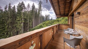 Une terrasse en bois avec une table et des chaises, donnant sur une colline boisée.