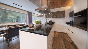Une cuisine moderne dotée d’un îlot central, d’un plafond en bois et de grandes fenêtres offrant une vue sur l’extérieur.