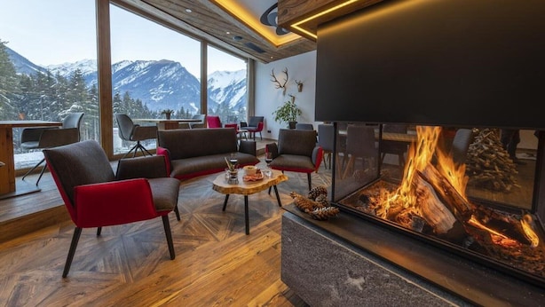 Un salon moderne doté d’une cheminée, de grandes fenêtres et offrant une vue sur des montagnes enneigées.