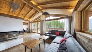 A modern interior with a wooden ceiling, a sofa, a dining table, and large windows offering a mountain view.