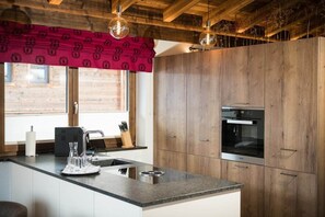Cozinha moderna com armários de madeira, forno embutido e uma janela grande com cortina estampada vermelha.