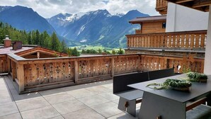 A wooden deck with a view of mountains, a table with chairs, and a wooden fence. - Stay near Ski Arena Wildkogel (Neukirchen)