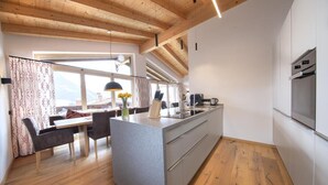 A modern kitchen with a central island, wooden flooring, and a view of the city through large windows. - Wellness Chalet near Wildkogel (Neukirchen)