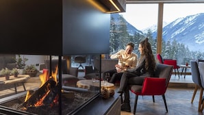 A modern living room with a fireplace, comfortable seating, and a view of snow-capped mountains.