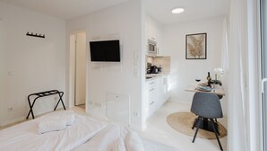 Une chambre moderne et bien éclairée, équipée d’un lit, d’un bureau et d’une kitchenette.