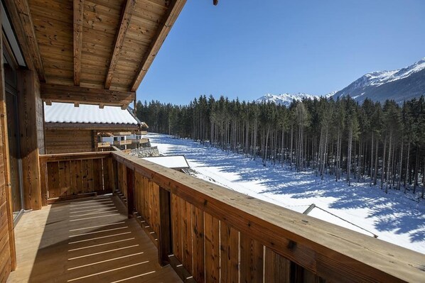 Una cabaña de madera con balcón que da a un bosque nevado y montañas.