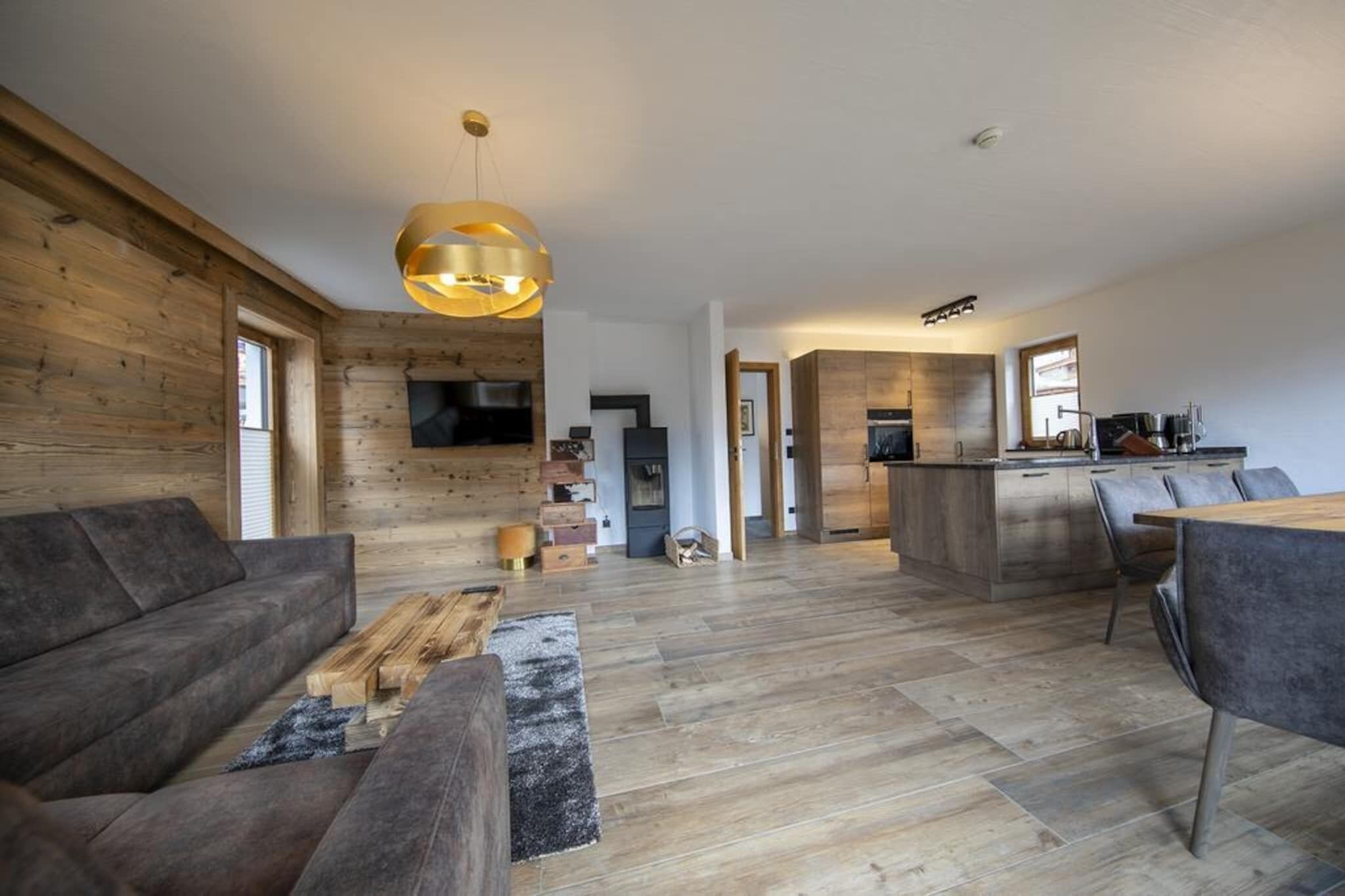 Ein großzügiges Wohnzimmer mit einer großen Couch, einem Couchtisch und Holzboden. Es gibt einen Küchenbereich mit einem Esstisch und Stühlen sowie eine moderne Pendelleuchte.