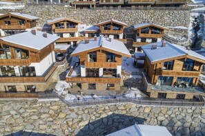 A cluster of wooden mountain chalets with stone foundations, each with a balcony and a view of the surrounding landscape.