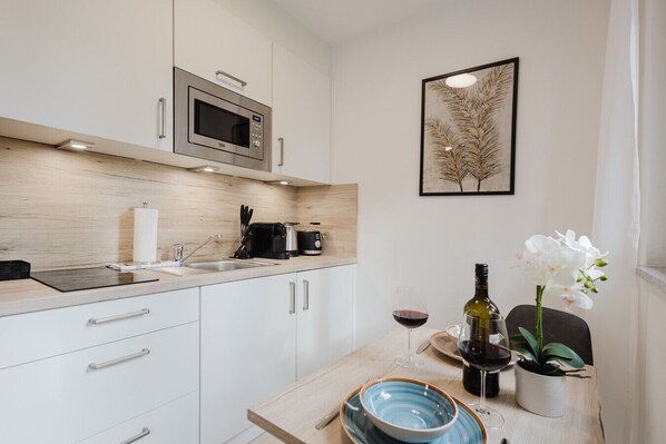 A modern kitchen with white cabinets, a microwave, a coffee maker, and a wine glass on the counter.