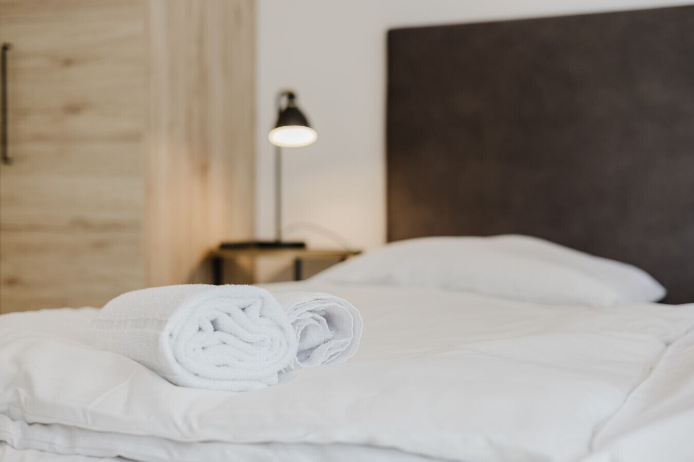 Un lit bien fait, avec du linge de lit blanc et une serviette enroulée posée sur le dessus.