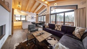 Un salon moderne avec un plafond en bois, un canapé, une table basse et une vue sur un balcon doté d’une balustrade en bois.