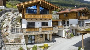 A modern chalet with a wooden balcony, stone walls, and a mountain backdrop. - Chalet with Sauna Near Ski Bus (Neukirchen)