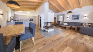 A spacious living area with a wooden ceiling, a fireplace, a dining table with chairs, and a sofa. - Chalet with Sauna Near Ski Bus (Neukirchen)