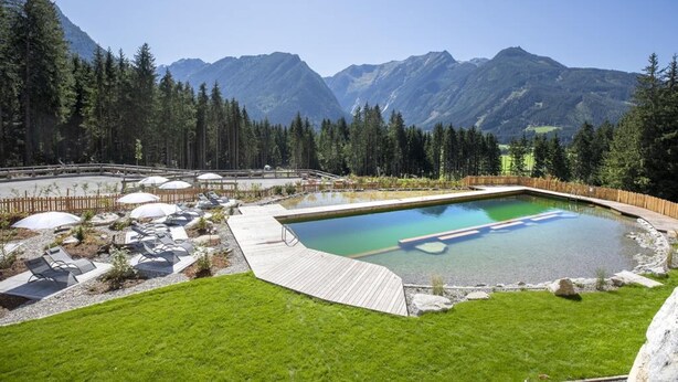 A swimming pool with a wooden deck, surrounded by a wooden fence, and a view of mountains in the background. - Chalet with sauna, Neukirchen (Neukirchen)