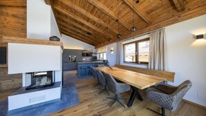 A modern kitchen with a central island, wooden flooring, and a dining area with a long table and chairs. - Chalet with sauna, Neukirchen (Neukirchen)