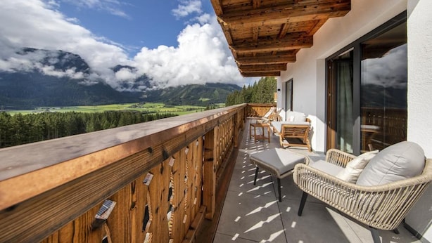 A balcony with a wooden railing, wicker furniture, and a view of mountains and a lake. - Stay near Ski Arena Wildkogel (Neukirchen)