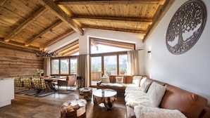 A spacious living room with a high ceiling, wooden beams, a large window, and a cozy seating area. - Stay near Ski Arena Wildkogel (Neukirchen)