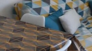 A dining area with a table and chairs, a sofa with patterned cushions, and a wall-mounted light fixture.