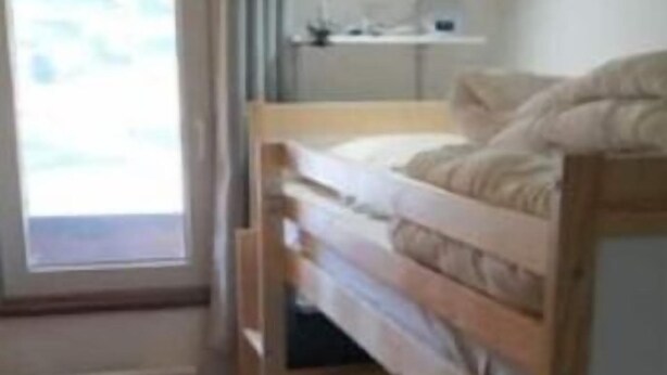A bunk bed room with a window, a desk with a lamp, and a shelf above the bed.