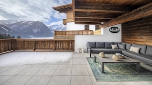 Ein modernes Wohnzimmer mit grauem Sofa, Holzboden und Blick auf schneebedeckte Berge.