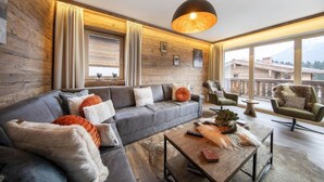 Ein modernes Wohnzimmer mit einem grauen Ecksofa, einem Holztisch und einem großen Fenster mit Vorhängen.