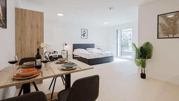 Une chambre d’hôtel moderne avec un coin repas, un lit doté d’une tête de lit bleue et une grande fenêtre.