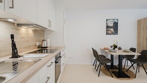 Une cuisine moderne avec des meubles blancs, un plan de travail en bois et un coin repas comprenant une table et des chaises.