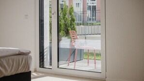 Une pièce dotée d’une porte-fenêtre coulissante qui donne sur un espace extérieur aménagé avec une chaise rouge et une petite table.