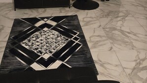 A room with a flat-screen TV on a stand, a black fan, a patterned rug, and a black sofa.