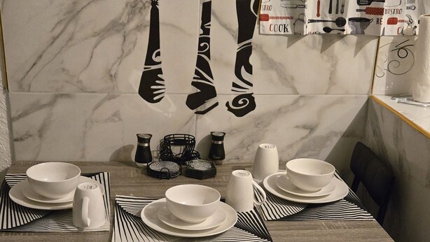 A dining table set with white plates, bowls, and a pitcher, with a black and white striped placemat.