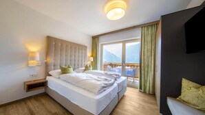 Ein Hotelzimmer mit einem großen Bett, einem an der Wand befestigten Fernseher und einem Balkon mit Bergblick.