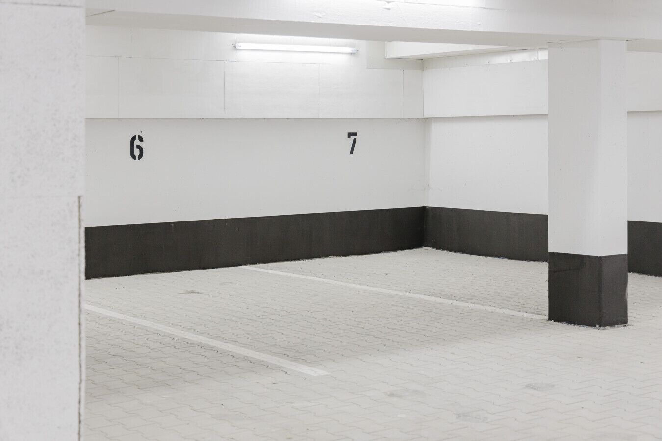 Un estacionamiento limpio y vacío con paredes blancas y zócalos negros, que muestra los espacios numerados 6 y 7.