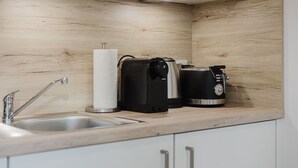 A modern kitchen with a wooden backsplash, a sink, a coffee maker, and a toaster. - The InnSight - Apartmenthouse (Passau)