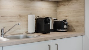 A modern kitchen with a wooden backsplash, a sink, a coffee maker, and a toaster. - The InnSight - Apartmenthouse (Passau)
