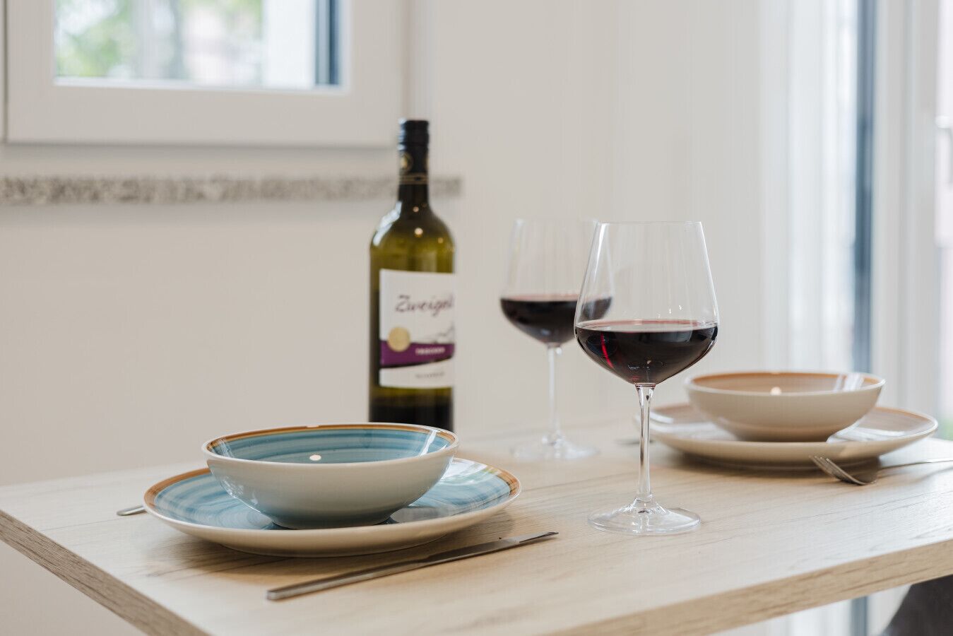 A dining table with a bowl, two wine glasses, and a bottle of wine.