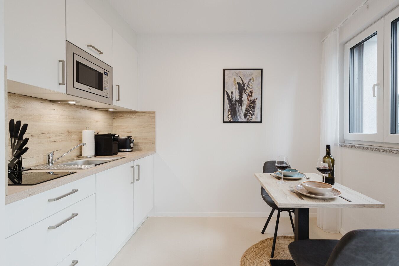 A modern kitchen with white cabinets, a built-in microwave, and a dining area with a table and chairs.