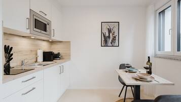A modern kitchen with white cabinets, a built-in microwave, and a dining area with a table and chairs.