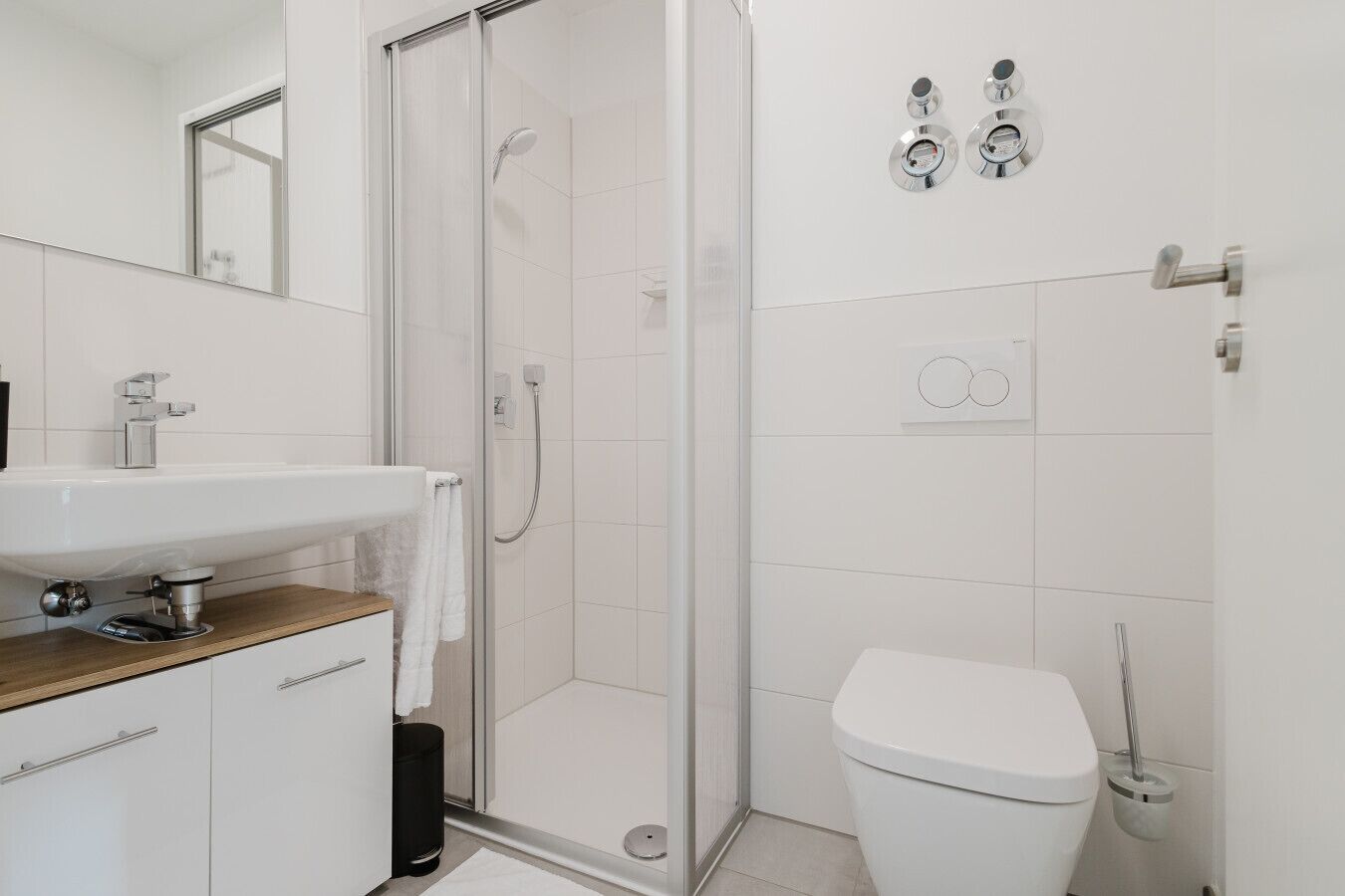 Een moderne badkamer met een douchecabine van glas, een witte wastafel en een toilet.