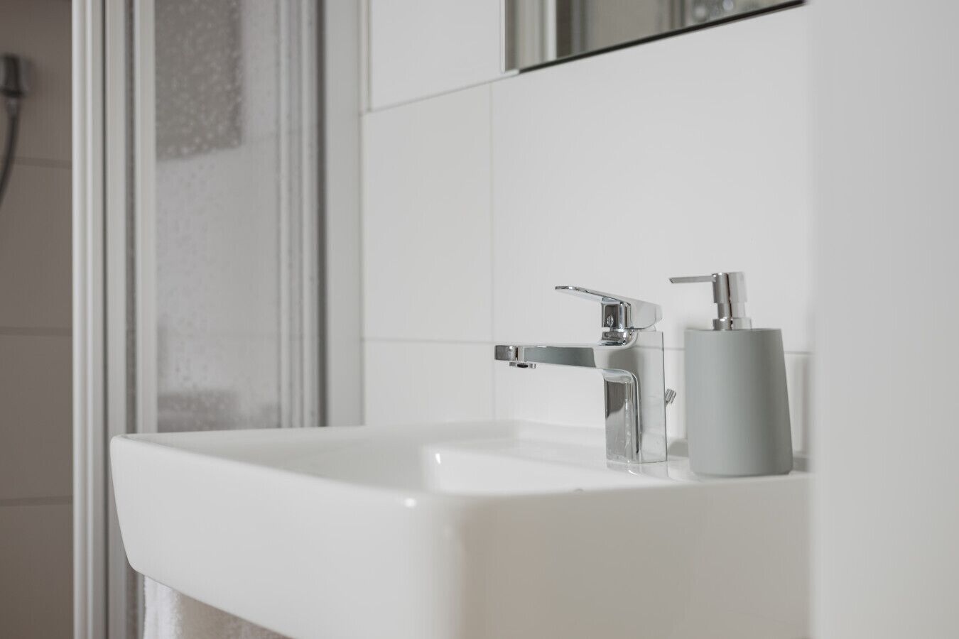Een moderne badkamer met een witte wastafel, chromefaucet en een zeepdispenser.