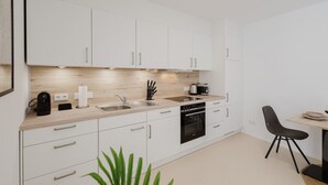 A modern kitchen with white cabinets, a wooden countertop, a built-in oven, and a dining area with a chair. - The InnSight - Apartmenthouse (Passau)
