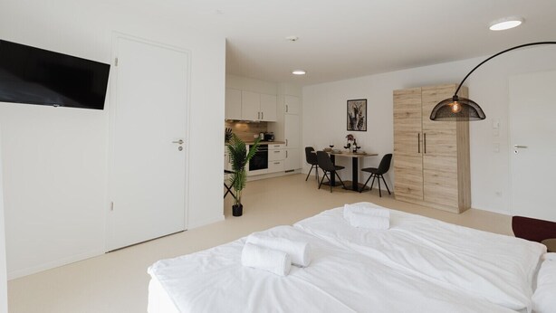 A modern hotel room with a large bed, a TV mounted on the wall, a dining area with a table and chairs, and a kitchenette. - The InnSight - Apartmenthouse (Passau)
